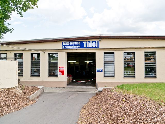 Werkstattgebäude mit dem Schild „Autoservice & Fahrzeughandel Thiel“ und offenem Tor