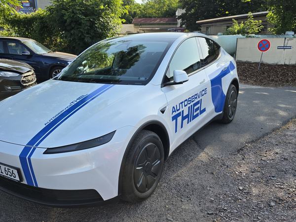 Weißer Tesla mit blauen Streifen und der Beschriftung „Autoservice Thiel“ an der Fahrertür